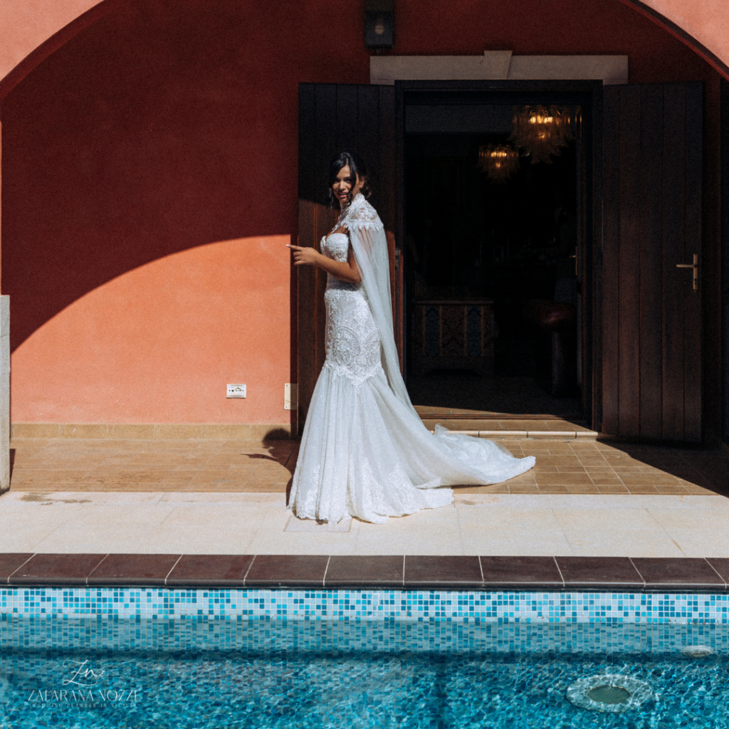 sposa con abito in piscina mentre sorride all'impiedi